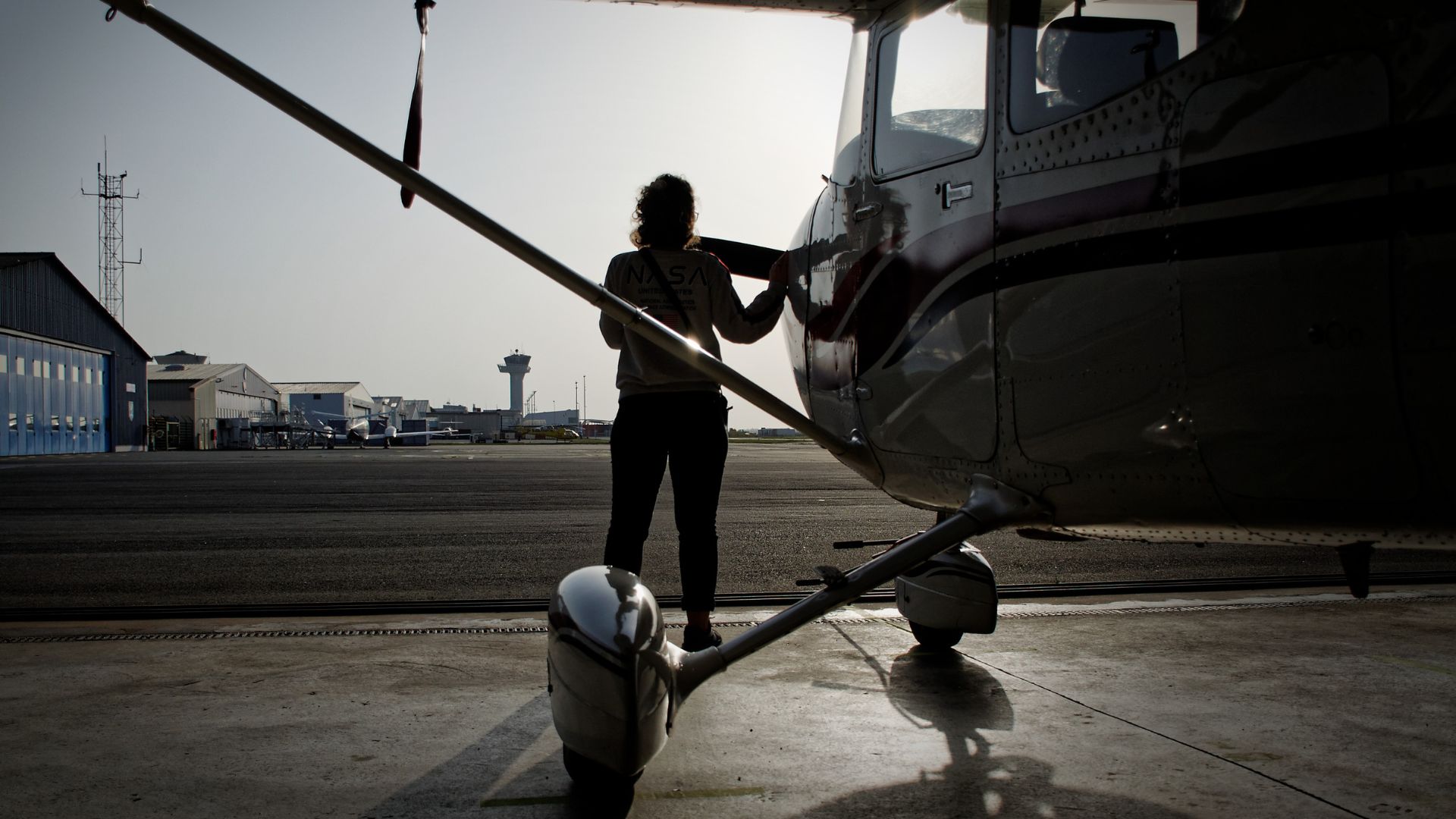 Silhouette of person preparing helicopter on airport tarmac at dawn