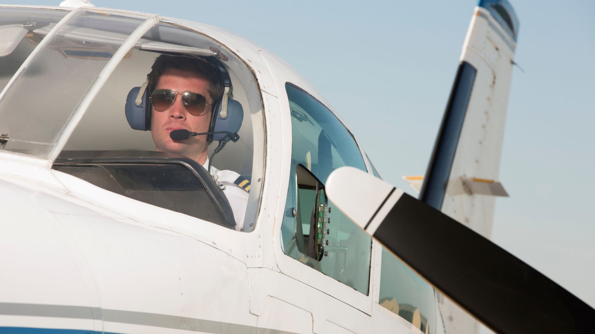 Pilot wearing headset and sunglasses sitting in cockpit of small aircraft