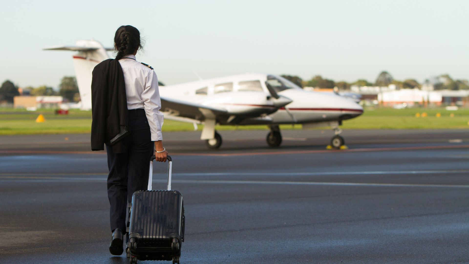 Pilot walking with luggage towards small aircraft on runway