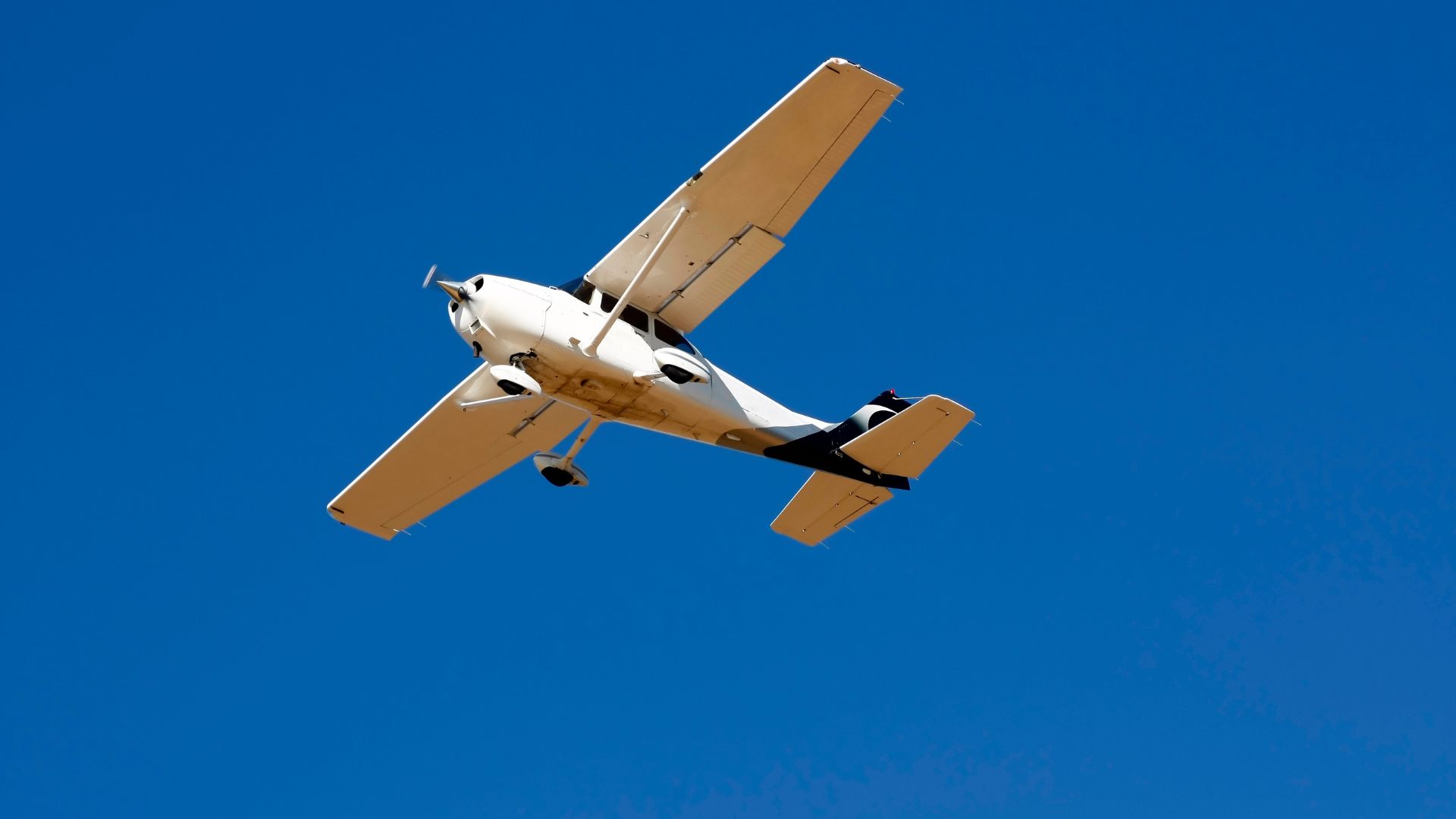 Small white and tan propeller plane flying against clear blue sky