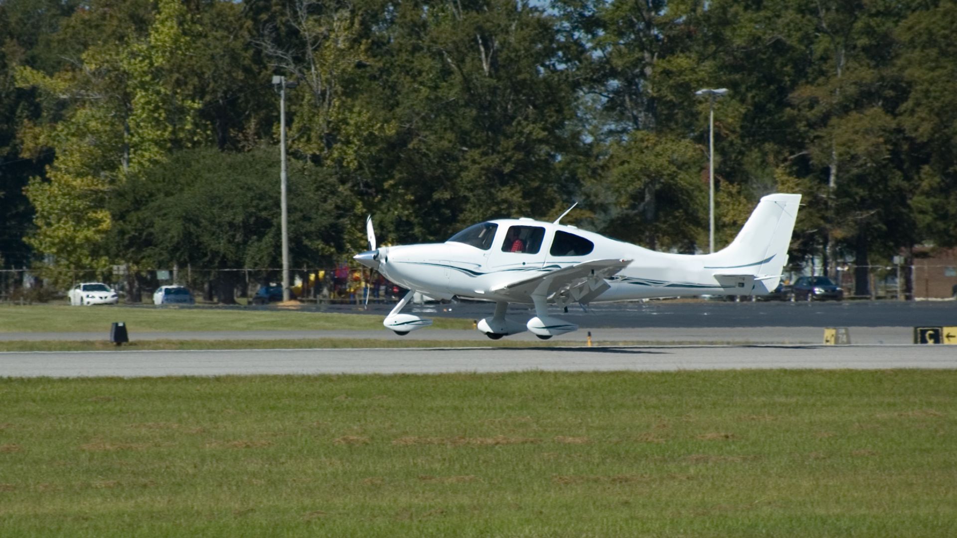 White small aircraft taxiing on runway with trees in background