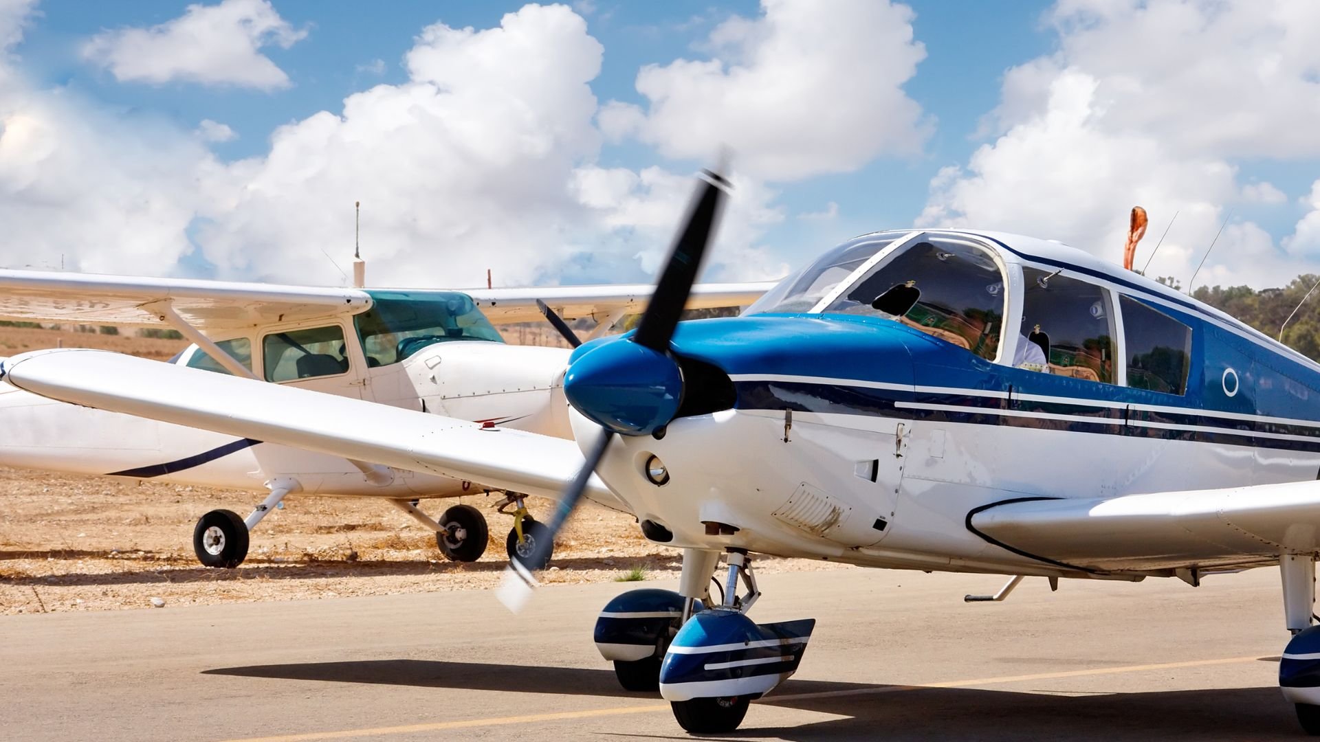 Two small propeller planes parked on a runway under fluffy clouds