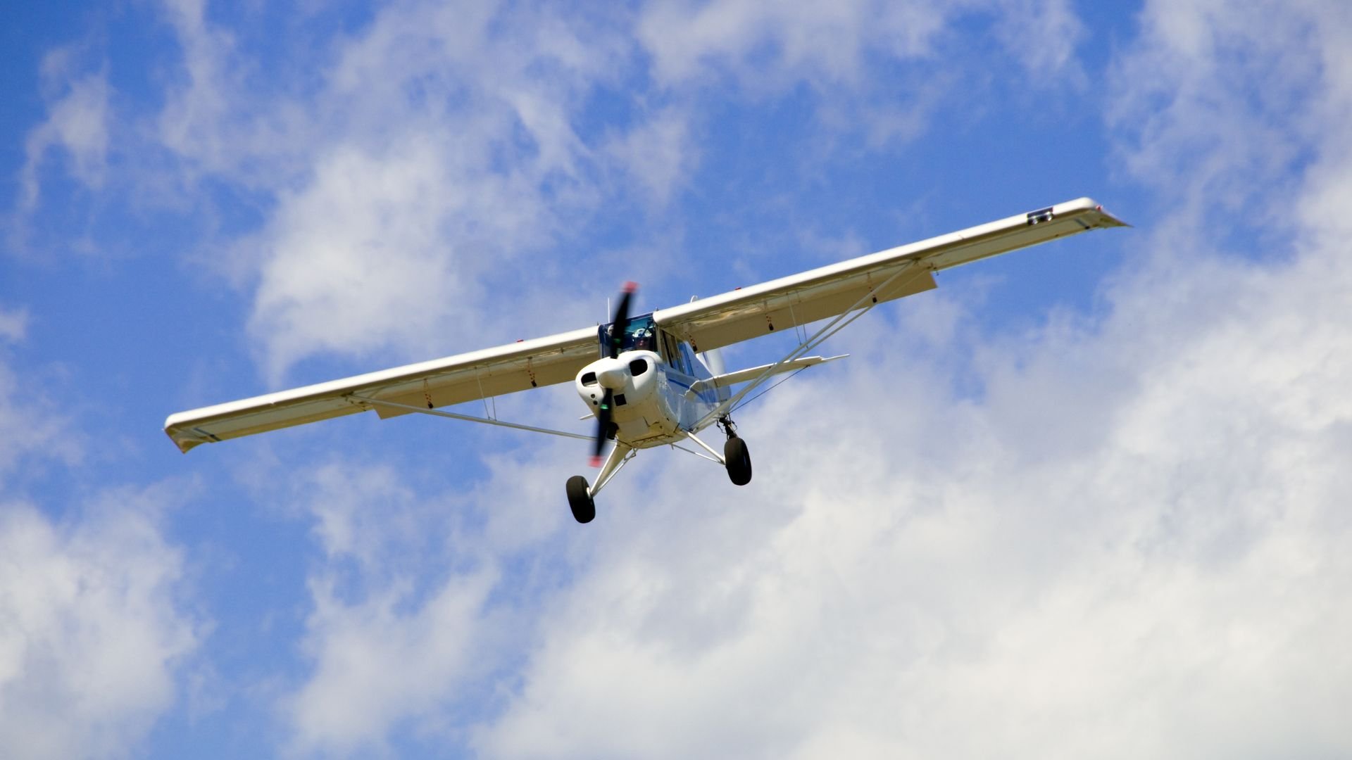 Small white propeller plane flying in cloudy blue sky